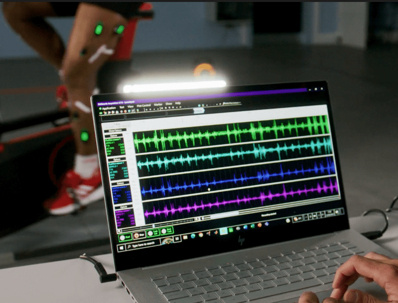 A laptop screen displays EMG signals with some cycling on an ergometer in the background